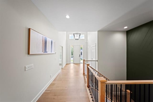 hall with a notable chandelier, light wood-style floors, recessed lighting, baseboards, and an upstairs landing