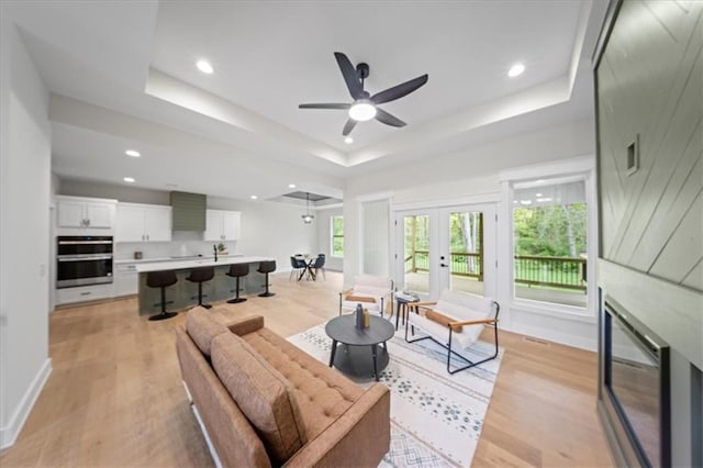 living room featuring light wood-style floors, ceiling fan, recessed lighting, a tray ceiling, and french doors