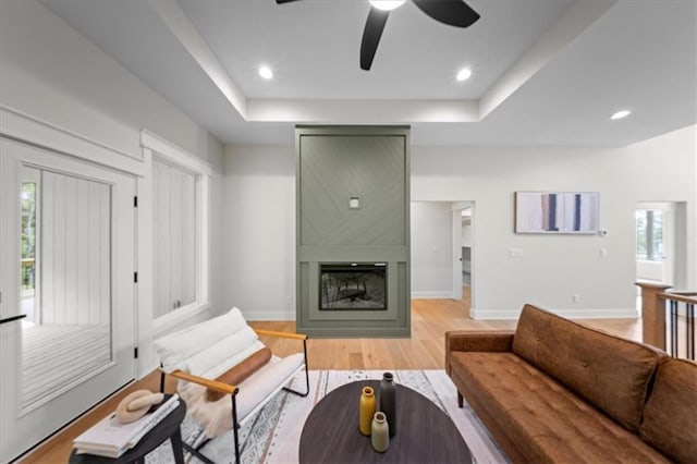 living room with a fireplace, baseboards, ceiling fan, a raised ceiling, and light wood finished floors