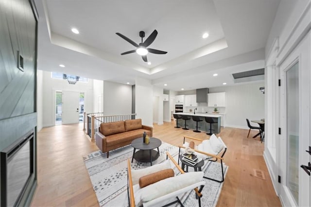 living area featuring baseboards, recessed lighting, a tray ceiling, a ceiling fan, and light wood-style flooring