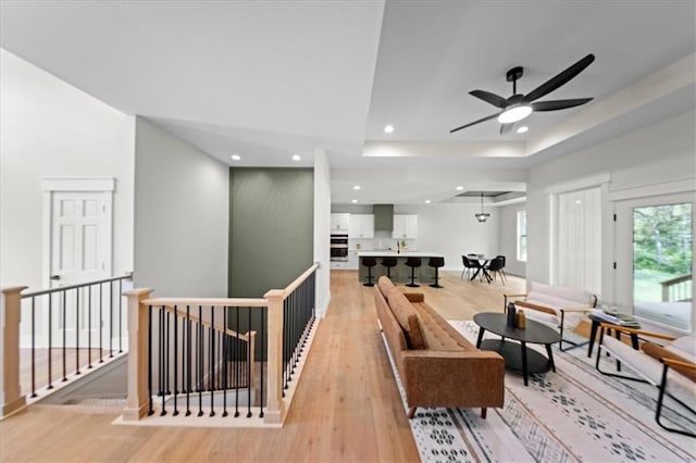 living area featuring recessed lighting, light wood-style flooring, ceiling fan, and a tray ceiling