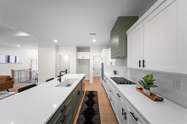 kitchen with white cabinets, a sink, light wood finished floors, light countertops, and black electric cooktop