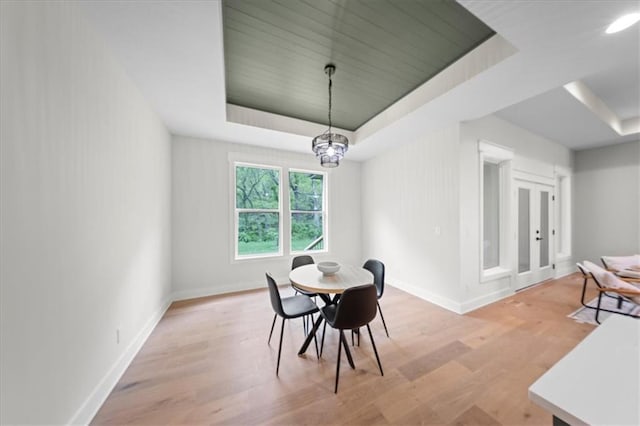 dining room with baseboards, a tray ceiling, and light wood finished floors