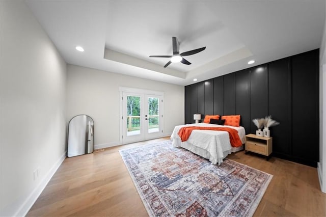 bedroom featuring french doors, access to exterior, a raised ceiling, baseboards, and light wood-style flooring