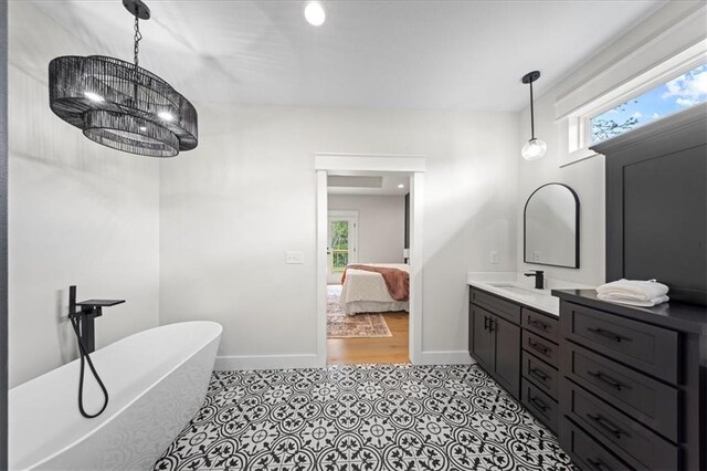 ensuite bathroom with plenty of natural light, a freestanding tub, a notable chandelier, and vanity
