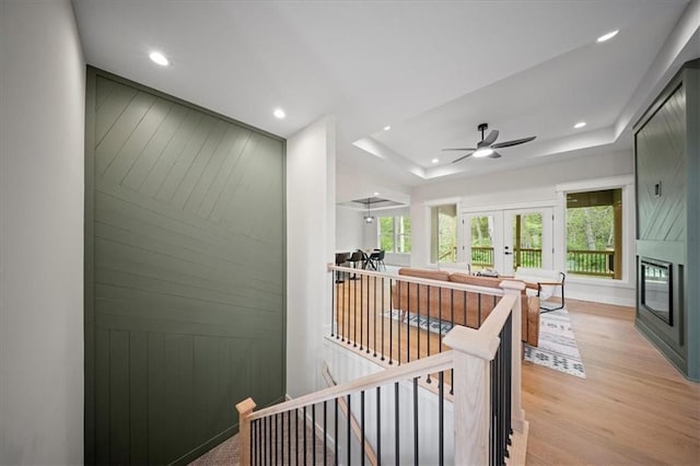 hallway with light wood finished floors, a raised ceiling, french doors, recessed lighting, and an upstairs landing