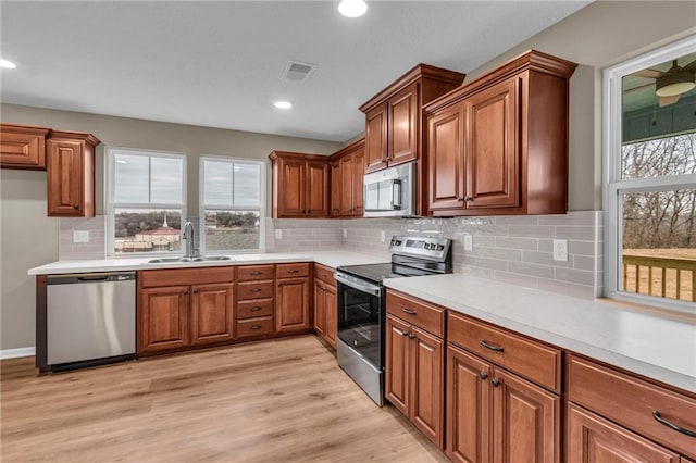 kitchen featuring visible vents, stainless steel appliances, a sink, a wealth of natural light, and brown cabinetry