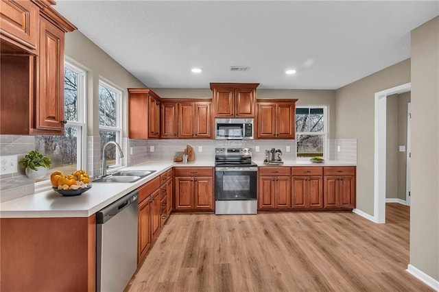 kitchen with a sink, stainless steel appliances, light wood finished floors, and brown cabinets