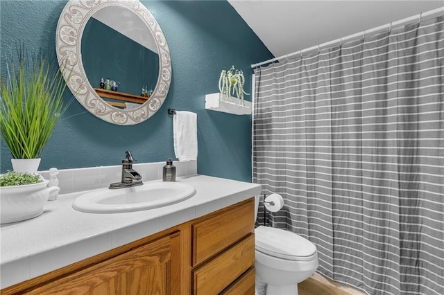 full bath featuring curtained shower, a textured wall, toilet, and vanity