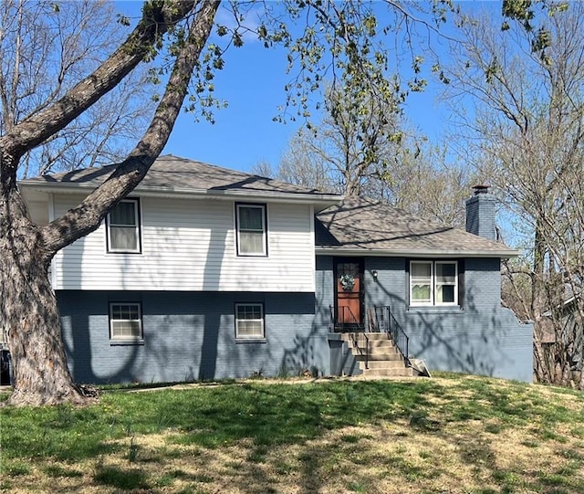 tri-level home featuring brick siding, a chimney, and a front lawn