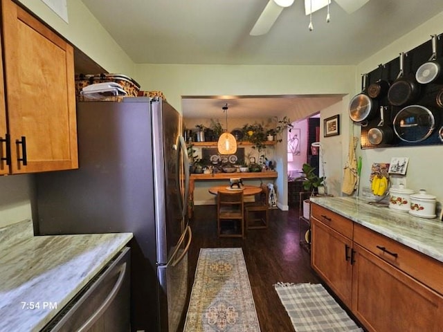 kitchen featuring ceiling fan, dark wood-style floors, brown cabinets, stainless steel appliances, and light stone countertops
