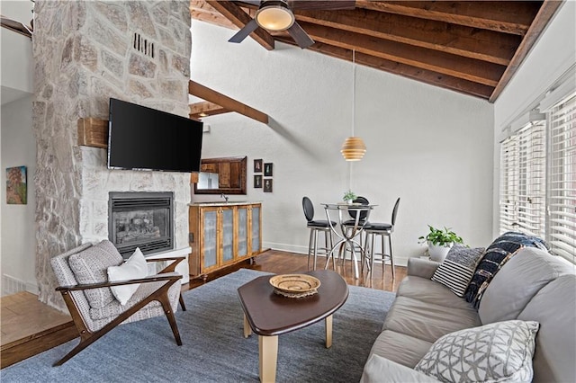 living area with ceiling fan, a fireplace, wood finished floors, baseboards, and lofted ceiling with beams