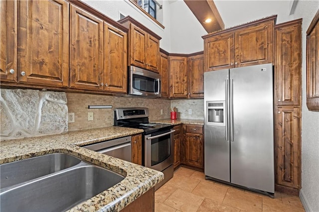 kitchen with a sink, appliances with stainless steel finishes, decorative backsplash, and light stone counters