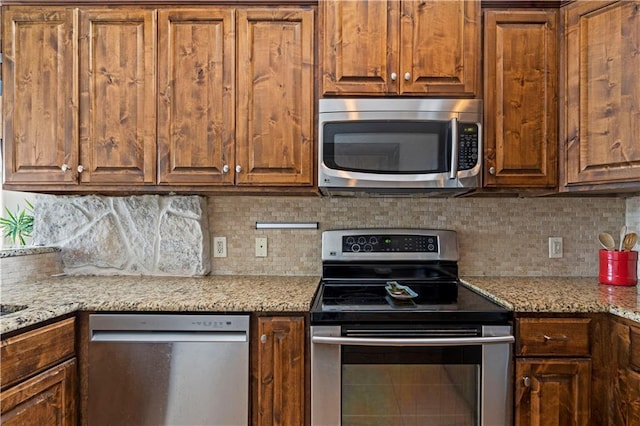 kitchen with stainless steel appliances, brown cabinetry, light stone counters, and decorative backsplash