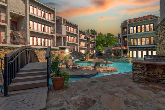 pool at dusk with a community pool and a patio