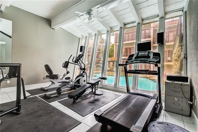 gym featuring vaulted ceiling, baseboards, a wall of windows, and a ceiling fan
