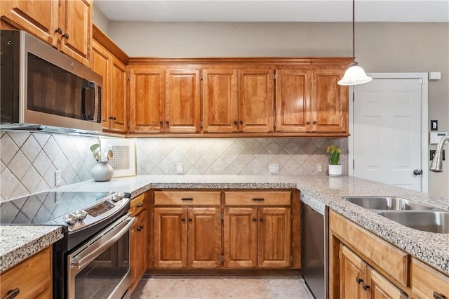 kitchen featuring brown cabinets, hanging light fixtures, a sink, and appliances with stainless steel finishes