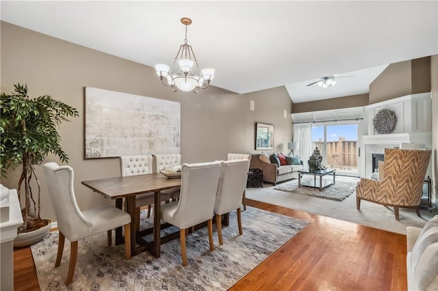 dining area with a fireplace, wood finished floors, vaulted ceiling, and ceiling fan with notable chandelier