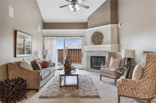 living area with a ceiling fan, high vaulted ceiling, a tiled fireplace, and visible vents