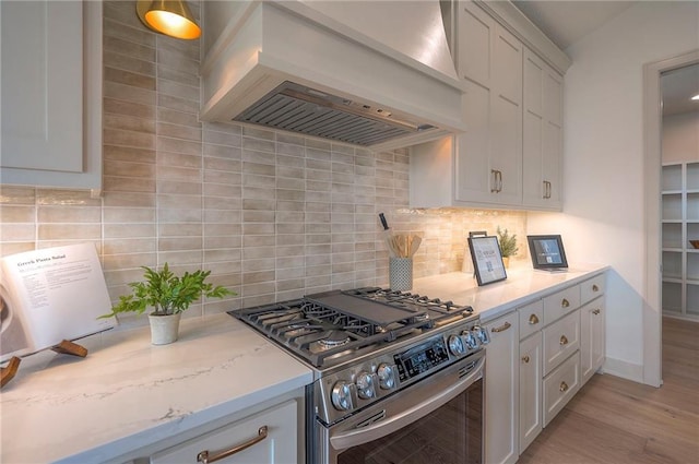 kitchen featuring tasteful backsplash, light wood-style floors, custom range hood, white cabinetry, and stainless steel range with gas cooktop