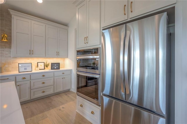 kitchen featuring white cabinetry, tasteful backsplash, stainless steel appliances, light countertops, and light wood-type flooring