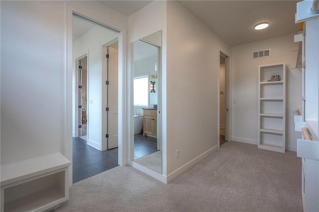 hallway with baseboards, visible vents, tile patterned flooring, and carpet