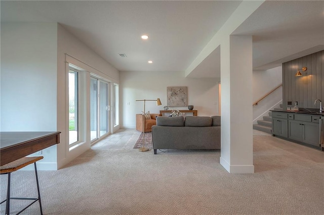 living room featuring stairs, visible vents, light carpet, and baseboards