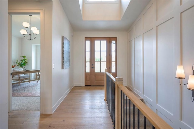 entryway featuring baseboards, light wood finished floors, and a notable chandelier
