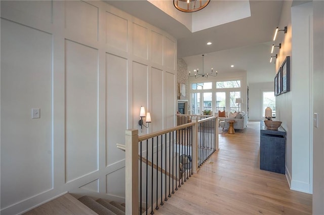 hallway with recessed lighting, a chandelier, an upstairs landing, light wood-style flooring, and a decorative wall