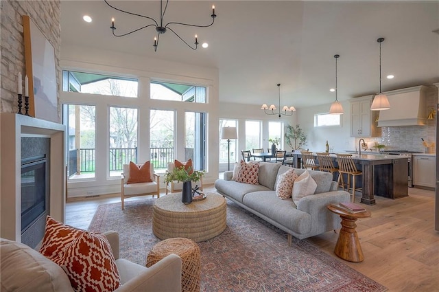 living area featuring a chandelier, a glass covered fireplace, light wood finished floors, and plenty of natural light
