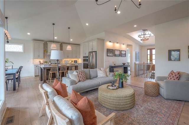 living area featuring a wealth of natural light, a chandelier, vaulted ceiling, and light wood-style floors