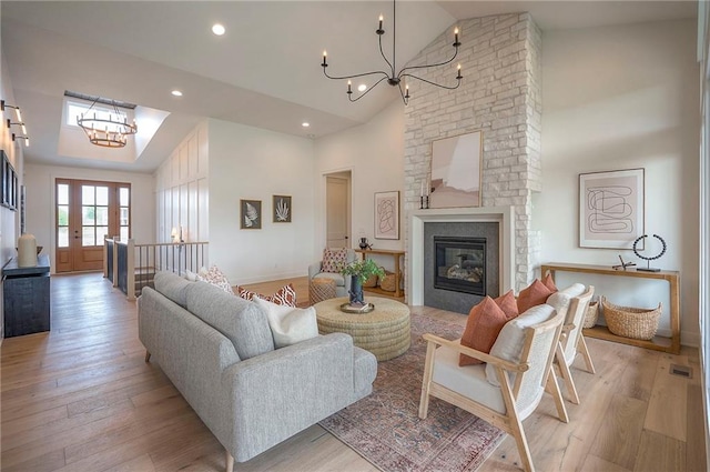 living room featuring a fireplace, light wood finished floors, high vaulted ceiling, and a notable chandelier