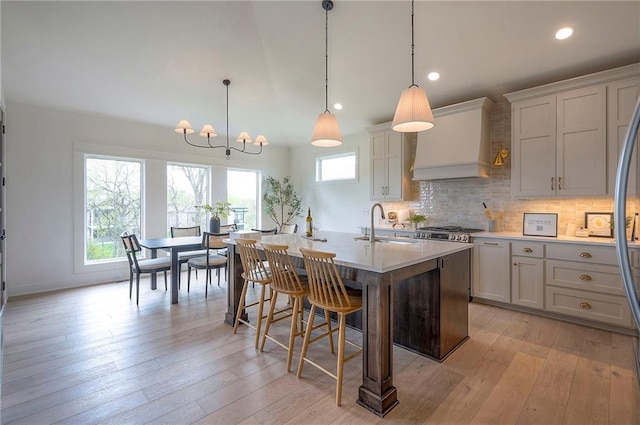 kitchen featuring an inviting chandelier, a sink, custom exhaust hood, backsplash, and light countertops