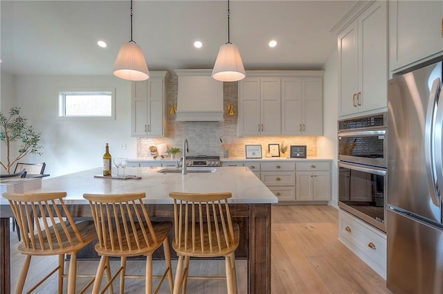 kitchen with light wood-style floors, appliances with stainless steel finishes, decorative backsplash, and premium range hood