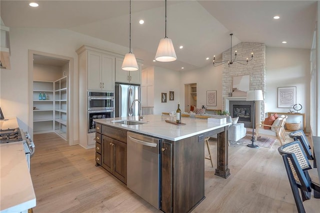 kitchen featuring appliances with stainless steel finishes, a kitchen bar, light wood finished floors, open floor plan, and a center island with sink