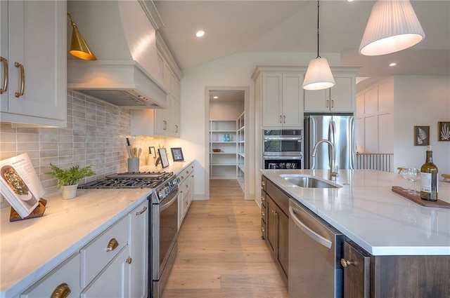 kitchen featuring a sink, a center island with sink, light wood-style flooring, premium range hood, and appliances with stainless steel finishes