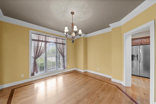 unfurnished room with a textured ceiling, baseboards, light wood finished floors, a notable chandelier, and ornamental molding