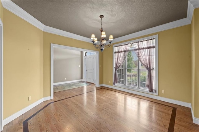 spare room featuring crown molding, wood finished floors, baseboards, a textured ceiling, and a chandelier
