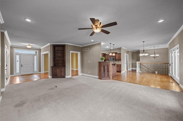 unfurnished living room featuring ornamental molding, ceiling fan with notable chandelier, visible vents, and light colored carpet