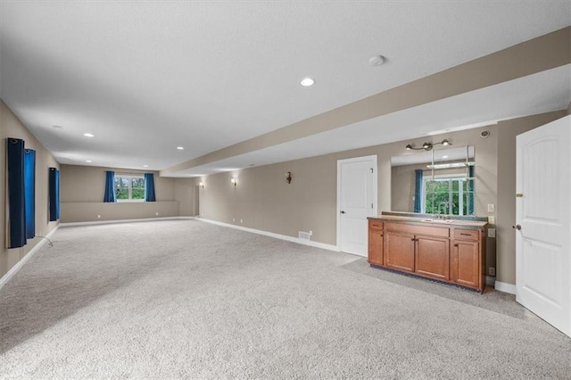 unfurnished living room with visible vents, baseboards, light colored carpet, recessed lighting, and a sink