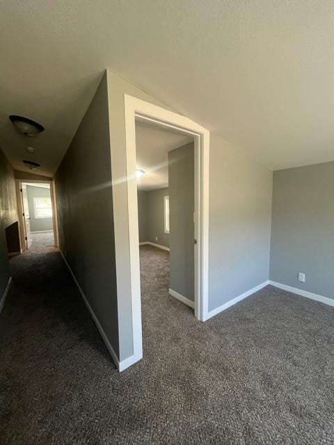 hall with baseboards, carpet floors, and vaulted ceiling