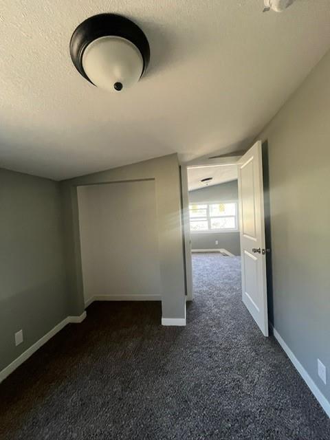 empty room featuring baseboards, lofted ceiling, dark colored carpet, and a textured ceiling
