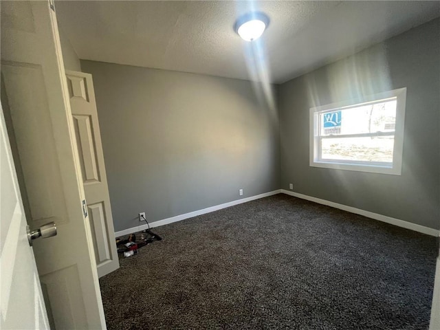 spare room with baseboards, dark colored carpet, and a textured ceiling