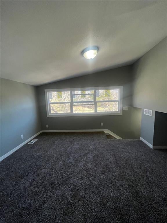 empty room featuring visible vents, baseboards, lofted ceiling, and dark carpet