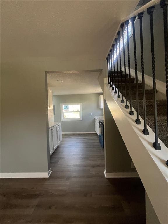 corridor featuring baseboards, stairs, a textured ceiling, and dark wood finished floors