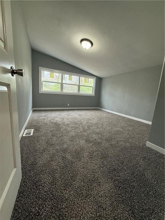 spare room featuring baseboards, visible vents, carpet floors, and vaulted ceiling