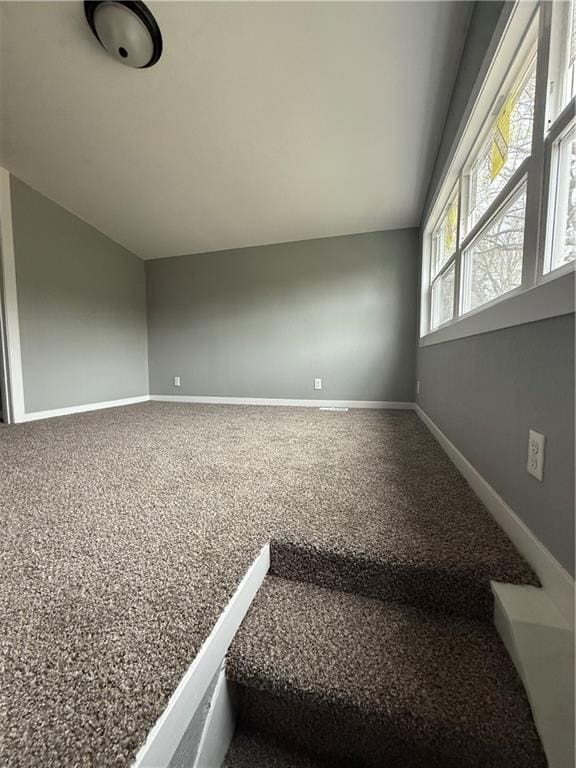 carpeted empty room with baseboards and vaulted ceiling