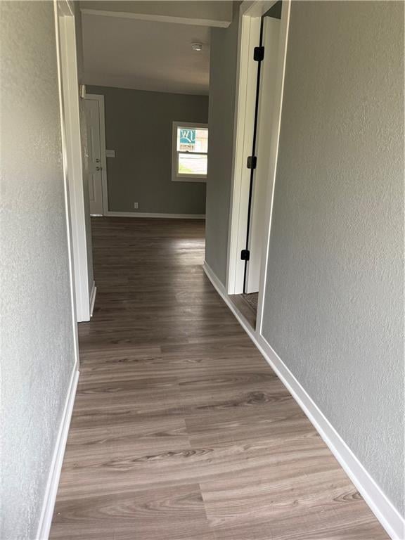 corridor featuring a textured wall, baseboards, and wood finished floors