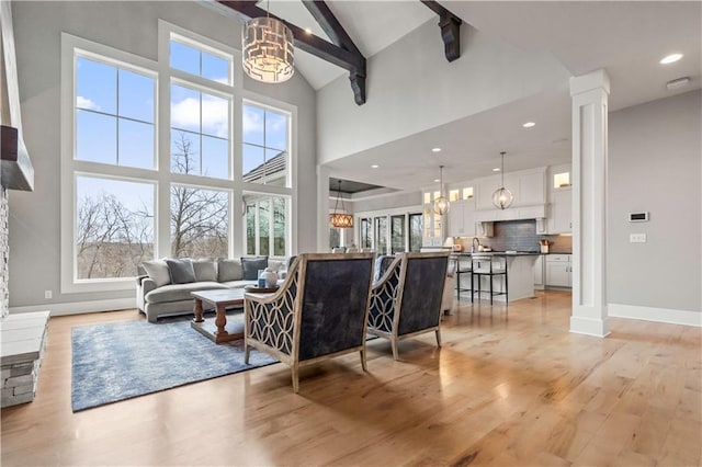 living room with a chandelier, light wood-style floors, high vaulted ceiling, beam ceiling, and baseboards