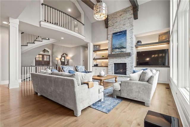 living area with a stone fireplace, high vaulted ceiling, wood finished floors, ornate columns, and beamed ceiling